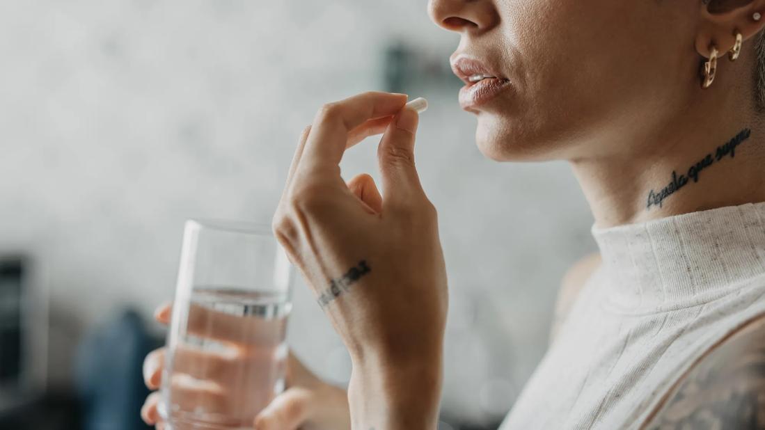 Person holding a glass of water, about to take a medication pill