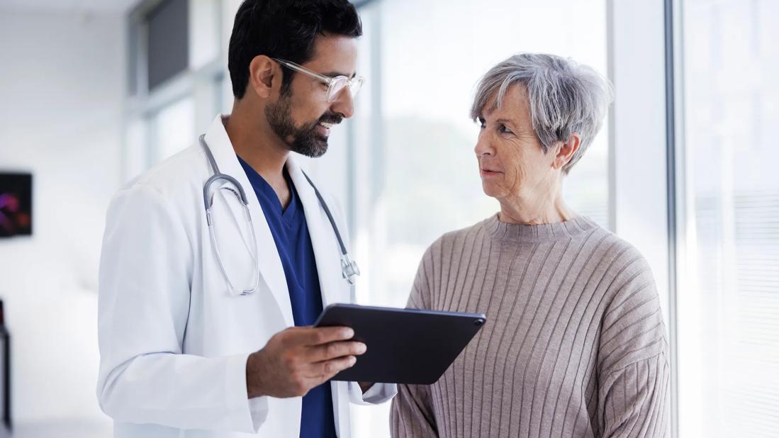 Healthcare provider holding a tablet, talking to patient in medical setting
