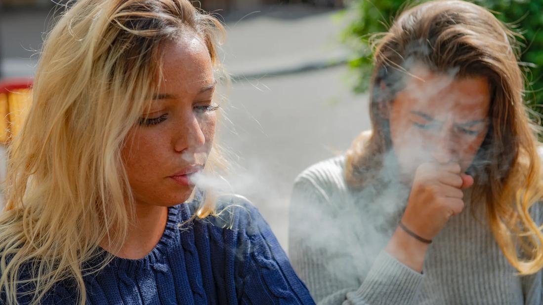 Person smoking in public, with secondhand smoke causing another person to cough