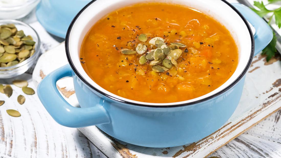 A light blue pot of lentil and pumpkin soup with pumpkin seeds and spices on top