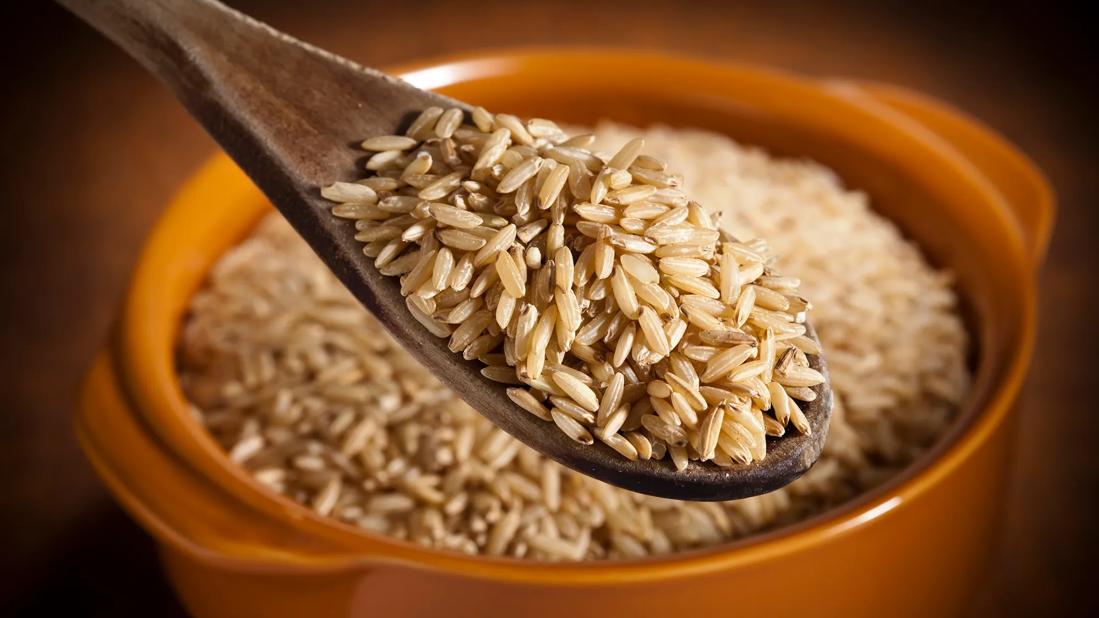 Wooden spoonful of brown rice over a slow cooker full of brown rice