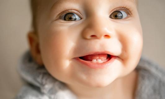 Smiling baby with big eyes and two tiny teeth