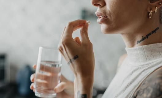 Person holding a glass of water, about to take a medication pill