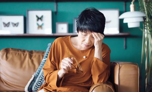 A stressed-looking woman sitting on couch, with hand on forehead