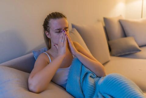 Person sitting on couch at night, pressing their hands on their nose/sinuses